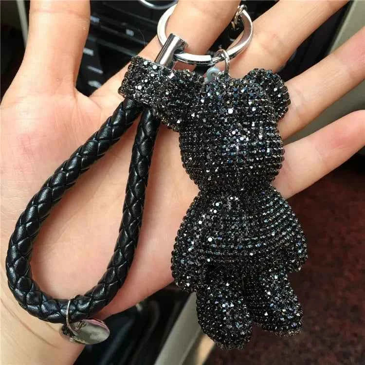 Black rhinestone bear keychain with braided leather strap held in hand
