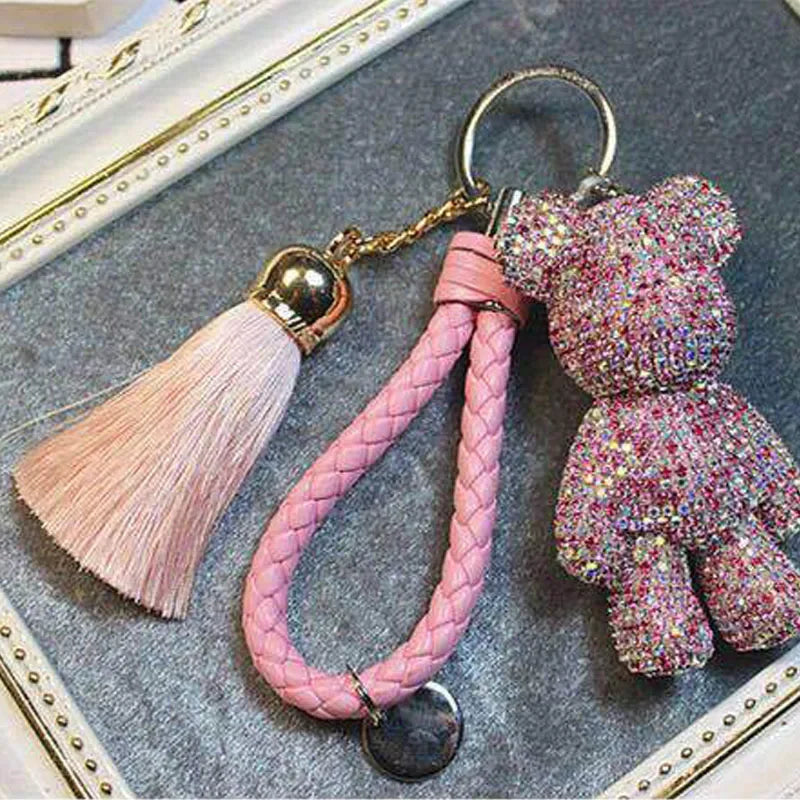Pink rhinestone bear keychain with braided strap and tassel accessory on a gray surface