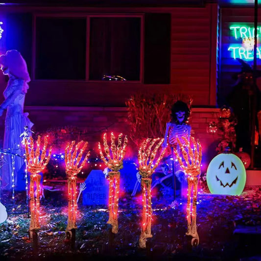 Halloween ghost hand lights glowing orange on skeletal hands in a spooky outdoor Halloween decoration setup