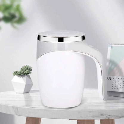 White automatic self stirring coffee mug with silver rim on marble table next to calendar and plant