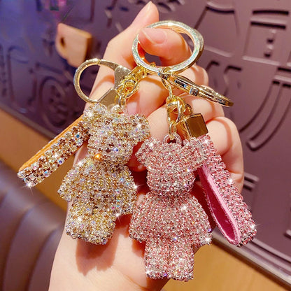 Two rhinestone bear keychain charms in gold and pink held in hand with matching rhinestone straps