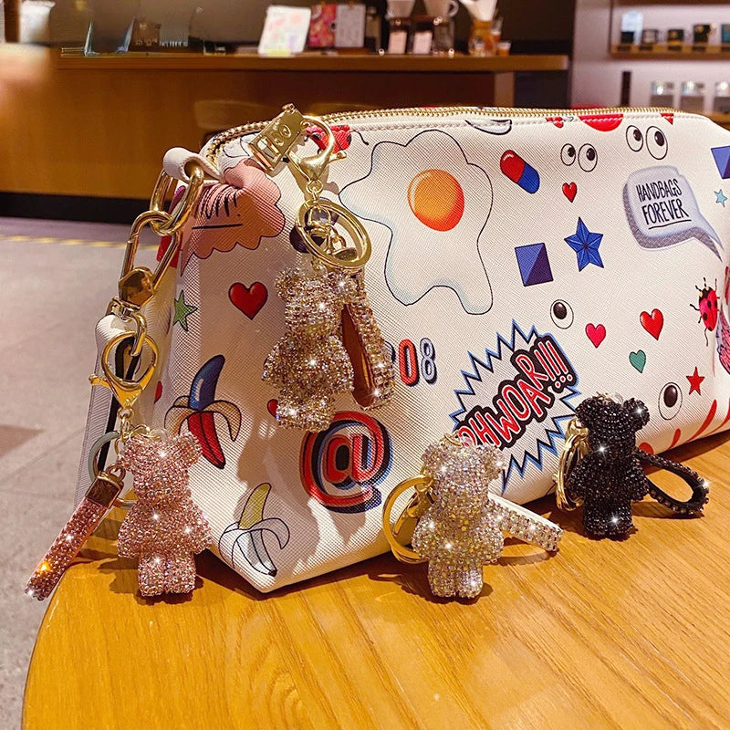 DFShop rhinestone bear keychain in various colors attached to colorful graphic pouch on wooden table