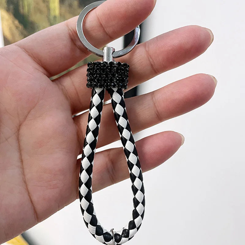 Hand holding a black and white braided loop keychain with a rhinestone adorned top piece