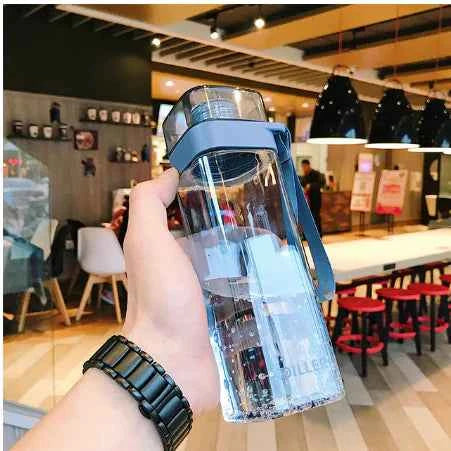 Hand holding a trendy square water bottle with blue cap and strap in a modern cafe setting
