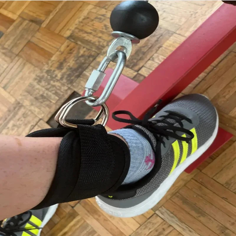 Close-up of double d-ring ankle straps for gym attached to a cable machine on a person wearing gray and yellow sneakers
