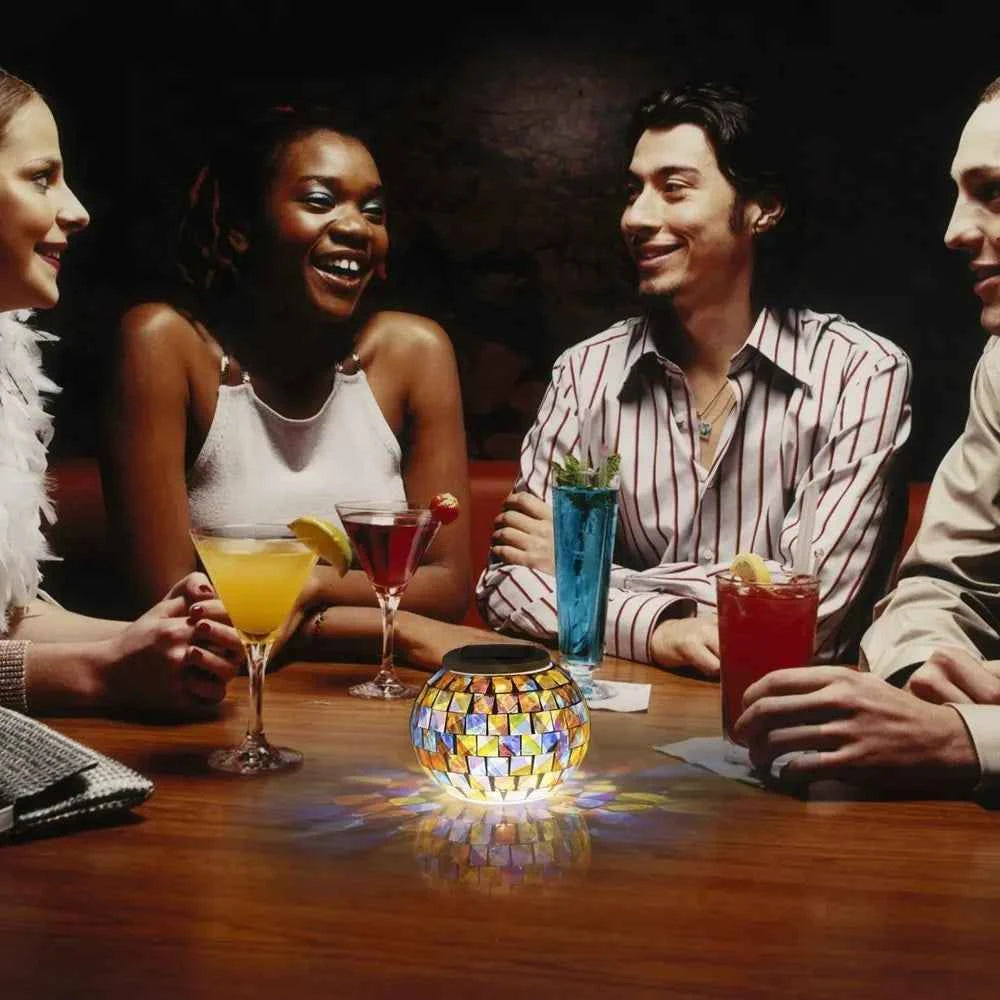 Colorful solar mosaic garden lights on table illuminating friends enjoying drinks in dim setting