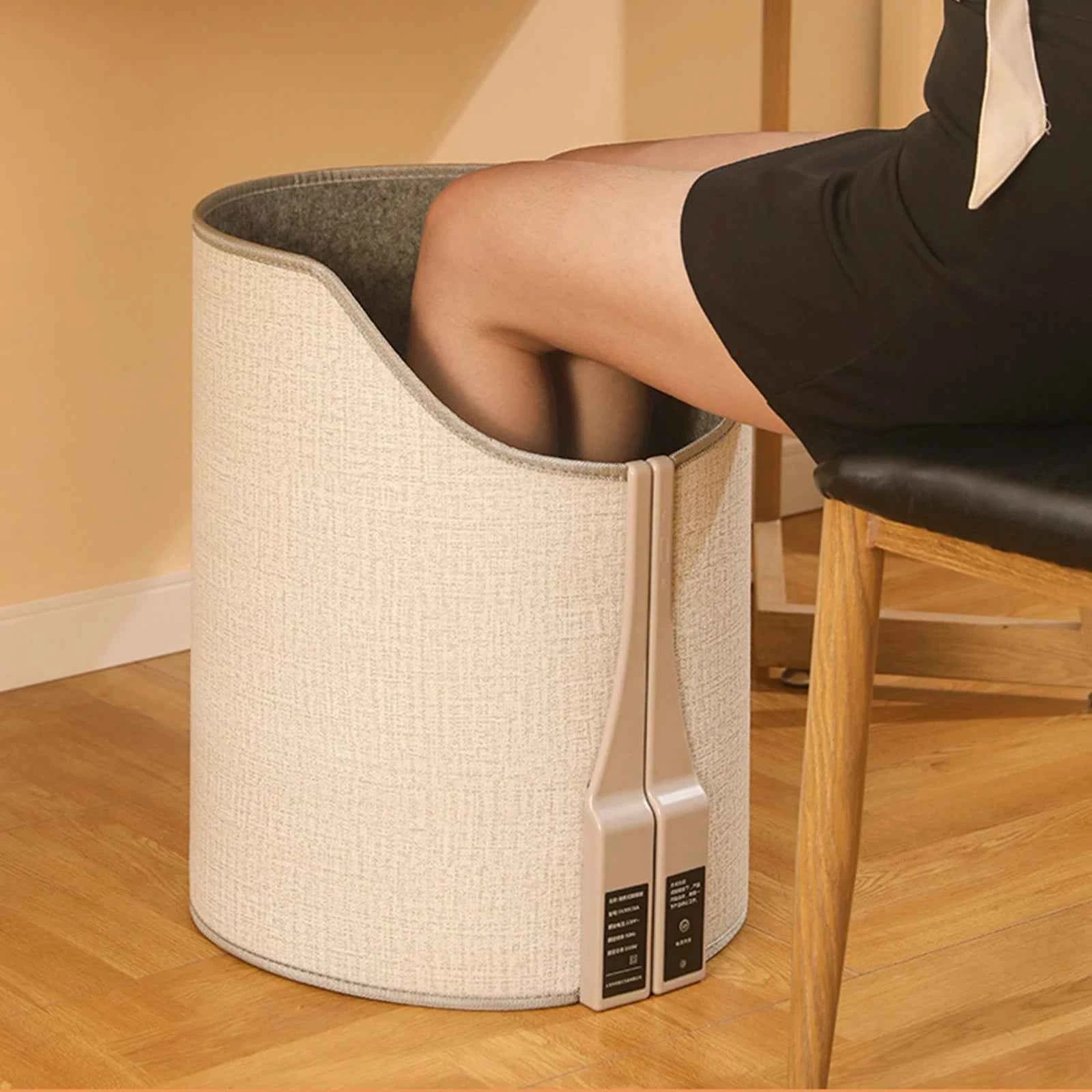 Portable heated foot warmer for home in beige fabric with a person using it while sitting on a chair