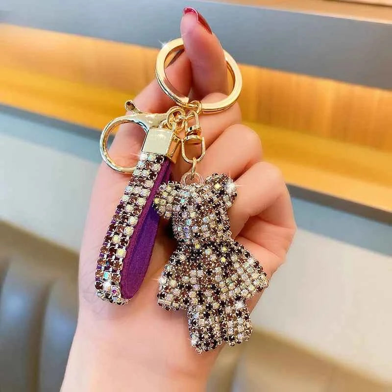 Hand holding a sparkling rhinestone bear keychain with a purple leather strap and gold key ring
