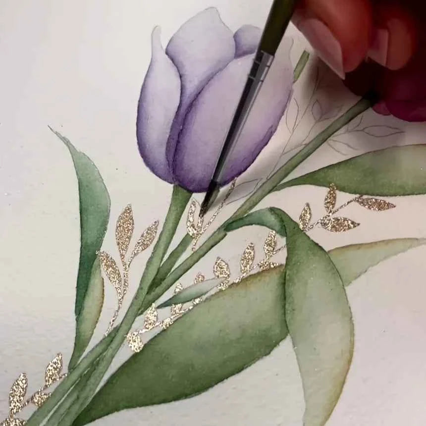 Artist using shifting watercolor painting set to create detailed purple flower with green leaves and gold accents