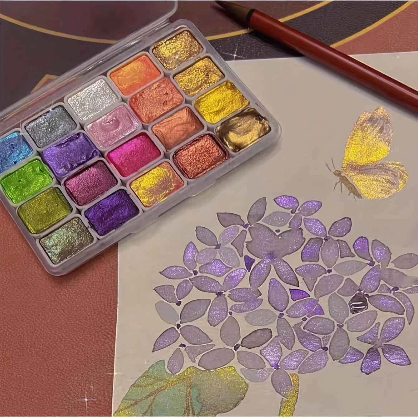 Shifting watercolor painting set with vibrant metallic colors and brush creating purple flowers and yellow butterfly artwork