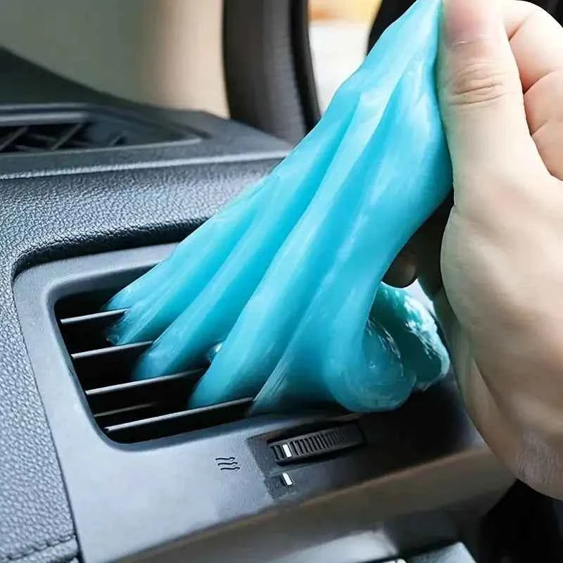 Blue car cleaning gel being used to clean a car air vent in a black dashboard interior